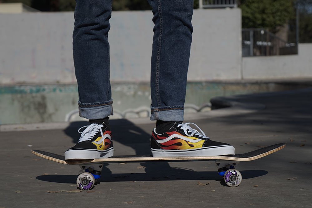 Legs shown standing on a skateboard wearing Vans Old Skool Flames sneakers