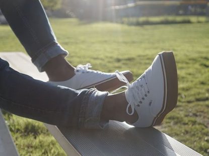Legs shown on metal bleachers wearing white and gum Vans Authentic shoes