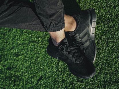 Guy’s feet shown wearing black NMD sneakers from adidas, resting on green turf